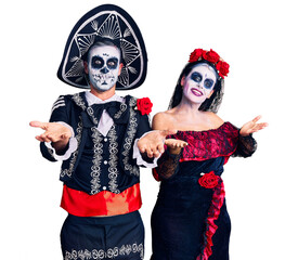 Wall Mural - Young couple wearing mexican day of the dead costume over background smiling cheerful with open arms as friendly welcome, positive and confident greetings