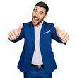 © Krakenimages.com - Young hispanic man wearing business jacket approving doing positive gesture with hand, thumbs up smiling and happy for success. winner gesture.