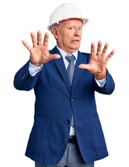 Poster - Senior handsome grey-haired man wearing suit and architect hardhat afraid and terrified with fear expression stop gesture with hands, shouting in shock. panic concept.