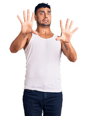 Poster - Young hispanic man wearing casual clothes afraid and terrified with fear expression stop gesture with hands, shouting in shock. panic concept.