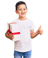 Wall Mural - Little cute boy kid holding gift smiling happy and positive, thumb up doing excellent and approval sign