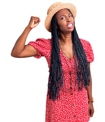 Canvas Print - Young african american woman wearing summer hat angry and mad raising fist frustrated and furious while shouting with anger. rage and aggressive concept.