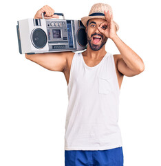 Wall Mural - Young hispanic man holding boombox, listening to music smiling happy doing ok sign with hand on eye looking through fingers