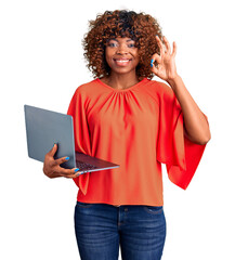 Sticker - Young african american woman working using computer laptop doing ok sign with fingers, smiling friendly gesturing excellent symbol