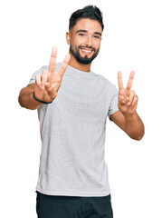 Wall Mural - Young man with beard wearing casual grey tshirt smiling looking to the camera showing fingers doing victory sign. number two.