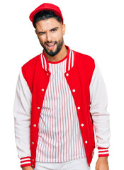 Canvas Print - Young man with beard wearing baseball uniform winking looking at the camera with sexy expression, cheerful and happy face.