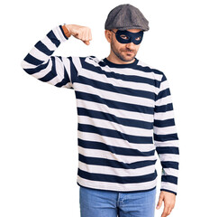 Sticker - Young handsome man wearing burglar mask strong person showing arm muscle, confident and proud of power