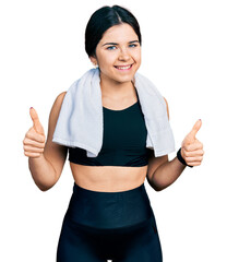 Young brunette woman with blue eyes wearing sportswear and towel success sign doing positive gesture with hand, thumbs up smiling and happy. cheerful expression and winner gesture.