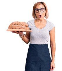 Canvas Print - Young blonde woman holding wholemeal bread scared and amazed with open mouth for surprise, disbelief face