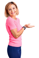 Sticker - Young blonde woman wearing sportswear pointing aside with hands open palms showing copy space, presenting advertisement smiling excited happy