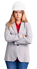 Poster - Beautiful young woman wearing architect hardhat skeptic and nervous, disapproving expression on face with crossed arms. negative person.