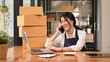 © Prathankarnpap - Young woman entrepreneur working in home office, preparing parcel boxes of product for delivery. Online selling, e-commerce concept