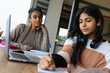 © Wavebreak Media - Biracial mother talking with teen daughter writing in book and studying over laptop on table at home