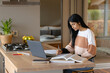 © Wavebreak Media - Biracial focused teenage girl writing in book while sitting with laptop on kitchen island at home