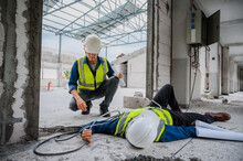 Accident At Work, An Asian Engineer Or Electrician Is Electrocuted To The Ground. A Colleague Engineer Rushed In For Help Or Assistance. Concept Of Accident At A Construction Site.