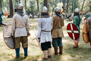 Vikings in helmets with weapons standing on the battlefield outdoors, rear view. Reconstruction of a medieval battle