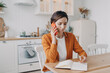 © VK Studio - Successful young woman is remote employee. Girl is sitting at table at kitchen and taking notes.