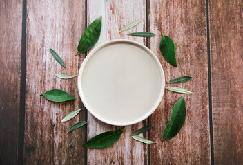 an empty beige ceramic plate surrounded by green leaves on a wooden background