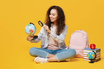 Full body happy young black teen girl student she wear casual clothes backpack bag loot at globe world map with loupe isolated on plain yellow color background. High school university college concept.