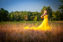 Beautiful And Sensual Young Caucasian Woman Wearing A Yellow Evening Dress Outside In A Natural Setting Over A Heather And Forest Background. High Quality Photo