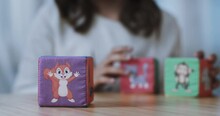 Three Children's Plush Cubes With Images Of A Squirrel, A Cat, A Mouse, A Monkey And A Rhinoceros. A Girl Holds The Cubes In Her Hands And Puts Them One On Top Of The Other. Close-up.