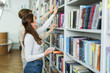© LIGHTFIELD STUDIOS - side view of teen girl in medical mask holding smartphone and choosing books near blurred friend.