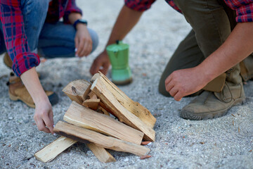 man and woman in camping kindling firewood in countryside for making coffee outdoors