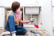 Woman sitting near leaking sink sking for help by phone