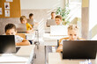 © Iryna - Education and school concept. Elementary school computer science class. Junior students girls and boys sitting at desk use laptops at lesson. Modern education concept.