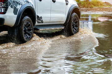 Pickup truck passing through flooded road. Driving car on flooded road during flood caused by torrential rains. Flooded city road with large puddle. Splash by car through flood water. Selective focus.