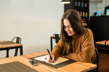 Female Freelancer Making Notes In Cafe