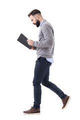 Wall Mural - Profile view of young bearded businessman walking while reading notebook or planner. Full body isolated on transparent background.