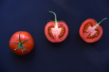 Wall Mural - Sliced and whole tomatoes on a black background. Juicy and delicious tomatoes close-up.