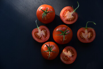 Wall Mural - Sliced and whole tomatoes on a black background. Juicy and delicious tomatoes close-up.