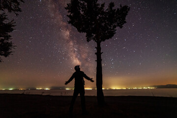 Wall Mural - Hiker silhouette stands on the shore on the milky way galaxy background. Dark starry night.