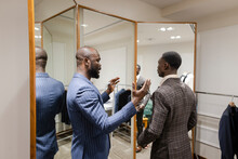 Tailor Talking With Customer Trying On Suit At Mirror In Menswear Shop