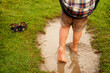 © CSRRDRGZ - Niño feliz jugando a columpiarse en el parque al aire libre mojando sus pies en el lodo en un charco de agua por la lluvia