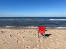 A Red Chair Standing Empty On The Beach Of The North Sea Under A Blue Sky