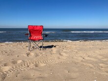 A Red Chair Standing Empty On The Beach Of The North Sea Under A Blue Sky