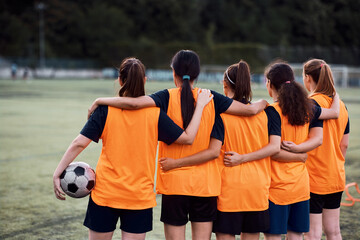 Rear view of embraced women's soccer team at stadium.