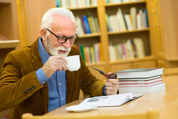 Wall Mural - Senior man reading book in the library