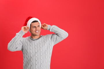 Wall Mural - Handsome man wearing Santa hat on red background, space for text