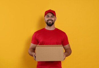 Wall Mural - Courier holding cardboard box on yellow background