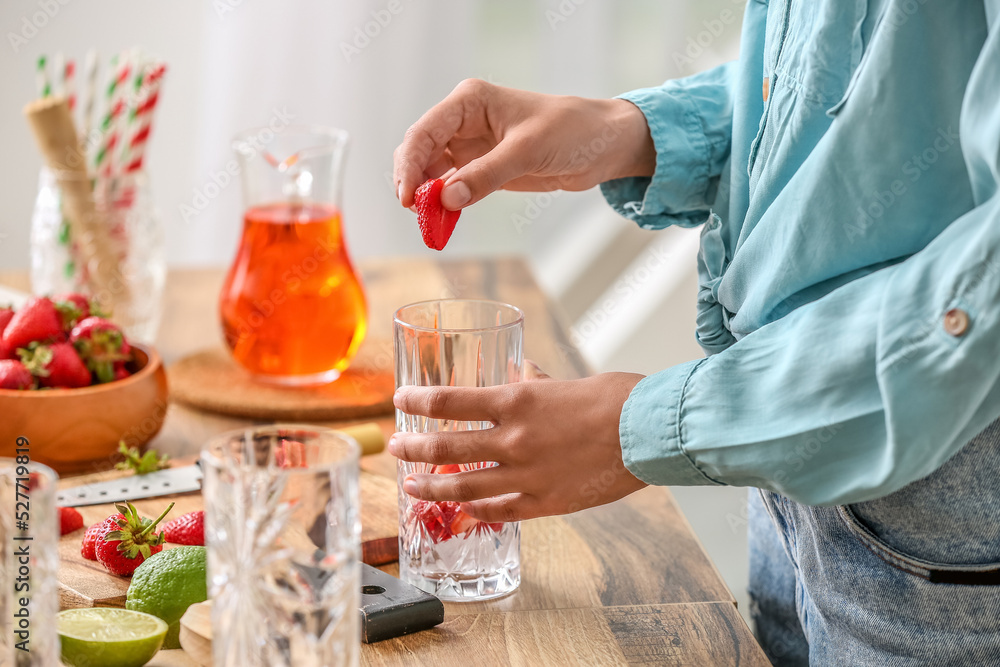 Woman preparing tasty strawberry lemonade in kitchen