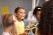 © WavebreakMediaMicro - Happy caucasian elementary schoolgirl sitting by multiracial female classmates during drawing class