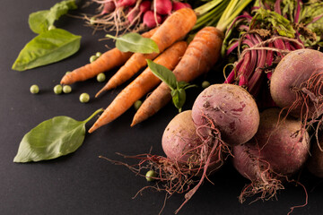 Close-up of carrots and beetroots with green peas and leaf vegetable on black background