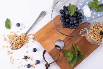 Wall Mural - Close-up of blue berries in bowl with granola and herbs on serving board over white background