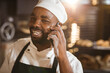 © Wavebreak Media - Smiling african american mid adult male baker talking on smart phone while standing in bakery