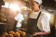 © Wavebreak Media - Asian mid adult female baker holding baking tray with croissant while working in bakery