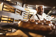 © Wavebreak Media - African american mid adult male baker keeping braided bread tray in rack